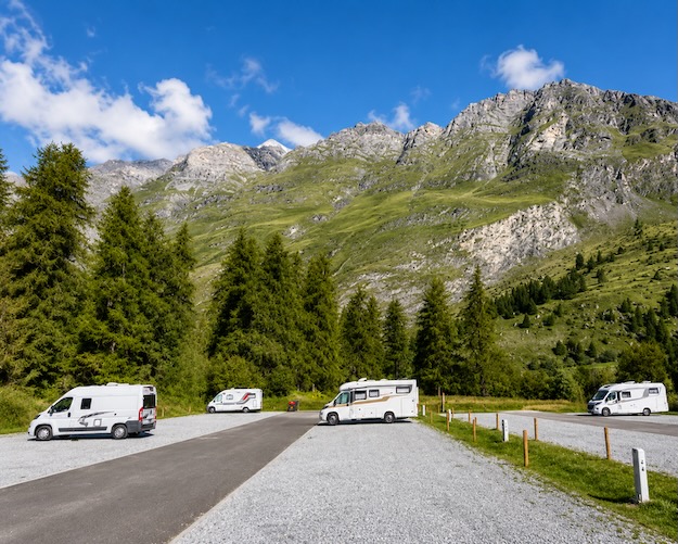 Wohnmobile in einer Berglandschaft mit grünen Wäldern und Bergen.